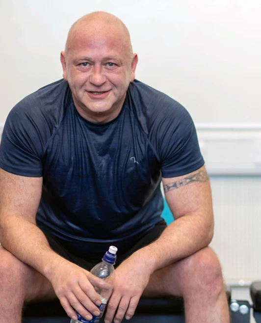 Man sitting on a gym bench, smiling and holding a water bottle after a workout. Man sitting on a gym bench, smiling and holding a water bottle after a workout.